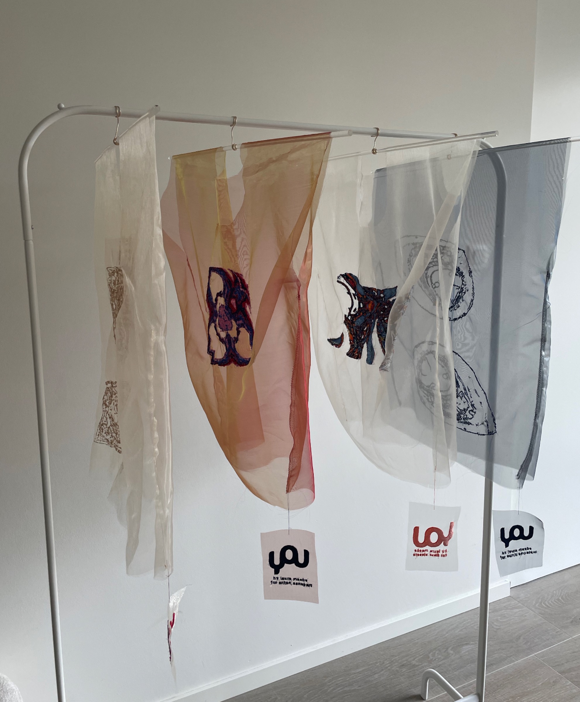 Exhibition display showing multiple YOU garments with unique embroidered designs